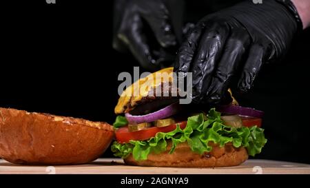 Handwerk Burger ist Kochen auf schwarzem Hintergrund. Bestehen: Sauce, Salat, Tomaten, Roten Zwiebeln, Gurke, Käse, Speck, Brötchen und marmoriertes Fleisch Rindfleisch. Stockfoto