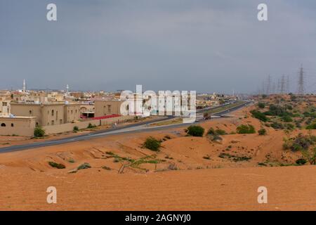 'Ras Al Khaimah, RAK/Vereinigte Arabische Emirate - 12/18/2019: Desert Storm clouds mit Fett verbrannt orange farbigem Sand gegenübergestellt und grün hinterlegt Flora Stockfoto