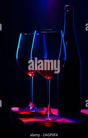 Zwei Gläser Rotwein mit Flasche auf Holztisch und dunklen Hintergrund. Intime Atmosphäre. Romantik Konzept Stockfoto