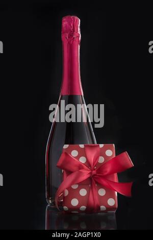 Flasche Rose Sekt mit romantischen Geschenk und roter Schleife. Vertikale Format. Auf schwarz isoliert. Champagner. Romantische vorhanden. Close Up. Stockfoto