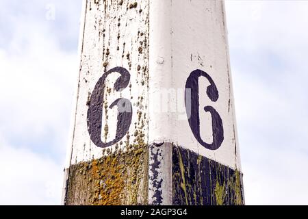 Horizontale Bild eines alten verwitterten Liegeplatz Post mit Nummer sechs auf jeder Seite gegen einen bewölkten Himmel gemalt Stockfoto