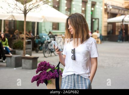 Modische junge Frau im weißen T-Shirt mit ihrem Telefon im Frühjahr in der Straße, Lifestyle Konzept Stockfoto