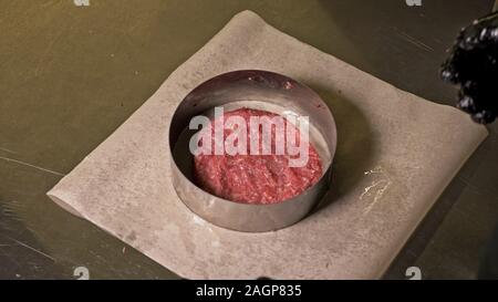 Kochen macht Fleisch Medaillons für Burger. Koch in schwarz Handschuhe macht Schnitzel essen. Die koteletts sind in Stahl Ring in eine noch Medaillon eingeebnet. Stockfoto