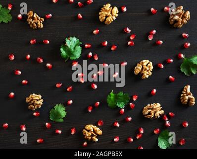 Essen Hintergrund. Granatapfel Samen, Nüsse und Koriander auf einem dunklen Hintergrund. Essen Muster. Flach, Ansicht von oben. Stockfoto