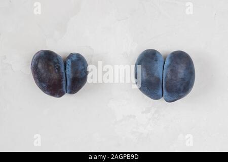 Trendy Hässliches Essen Konzept. Zwei violette Pflaumen auf grauem Hintergrund. Obst mit Herz Form. Das Problem von Speiseresten. Stockfoto