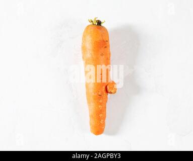 Trendy Hässliches Essen Konzept. Lustige Karotte auf einem weißen Hintergrund. Gemüse mit einer seltsamen Form. Das Problem von Speiseresten. Ansicht von oben, flach. Stockfoto