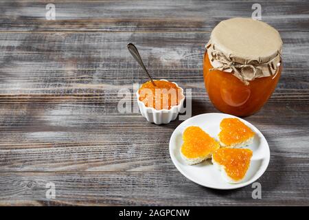 Hausgemachte Karotte Marmelade im Glas und Schüssel auf einem dunkelbraunen Holz- Hintergrund. Lecker Toast in der Form eines Herzens mit Karotte jam. Platz kopieren Stockfoto
