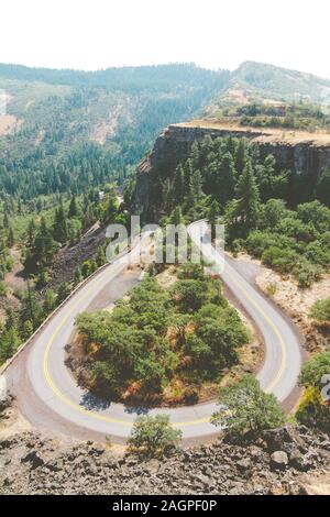 Einem hohen Winkel Blick auf einer kurvigen Straße auf Felsen durch Wälder mit Hügeln auf dem Hintergrund umgeben Stockfoto