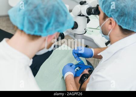 Arzt Mikroskop. Zahnarzt ist die Behandlung von Patienten in der modernen zahnmedizinischen Büro. Die Bedienung erfolgt mittels Fangdamms durchgeführt. Client wird eingefügt und wiederhergestellt Stockfoto