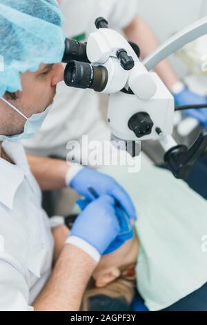 Arzt Mikroskop. Zahnarzt ist die Behandlung von Patienten in der modernen zahnmedizinischen Büro. Die Bedienung erfolgt mittels Fangdamms durchgeführt. Client wird eingefügt und wiederhergestellt Stockfoto