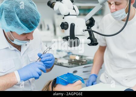 Arzt Mikroskop. Zahnarzt ist die Behandlung von Patienten in der modernen zahnmedizinischen Büro. Die Bedienung erfolgt mittels Fangdamms durchgeführt. Client wird eingefügt und wiederhergestellt Stockfoto