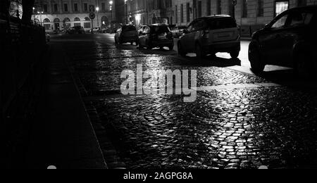 Regnerischen Nacht in der Stadt, feucht glänzende Kopfsteinpflaster mit parkenden Autos Stockfoto