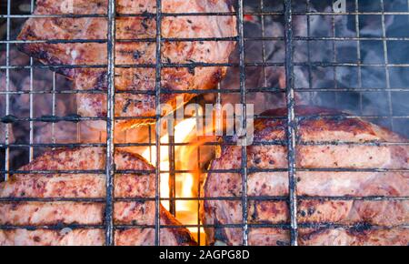 Paar Stücke etwas verbranntem Fleisch auf verkohlte Gitter mit Feuer und Rauch unter Stockfoto