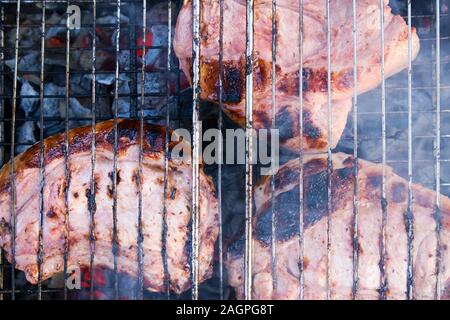 Paar Stücke etwas verbranntem Fleisch auf verkohlte Gitter mit Kohlen und Rauch unter Stockfoto