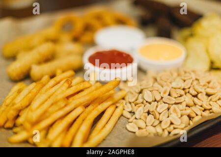 Lagerbier und Snacks auf Holztisch. Nüsse, Chips, Erdnüsse, Toast, Cracker. Vorspeise fast food. Handwerk Bier. Beerboard. Tomaten, Käse, Knoblauch Sauce. Stockfoto
