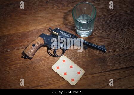 Russisches Roulette - sechs von Diamanten plaing Karte, Glas Wodka und Revolver mit einer Patrone in der Trommel auf hölzernen Tisch Hintergrund Stockfoto