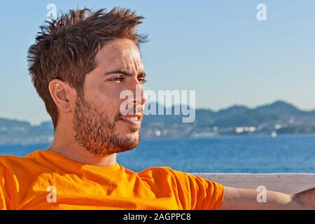 Ein junger zerzaust Rettungsschwimmer mit orange T-shirt am Strand rechts. Stockfoto