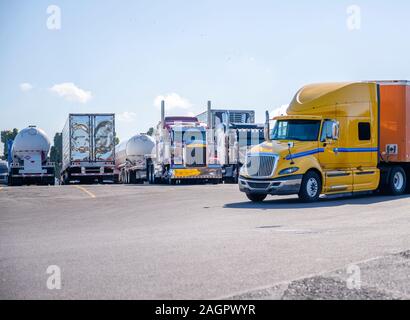 Big Rig gelb Long Haul Semi Truck mit Auflieger auf dem LKW-Parkplatz hinter dem Rest der semi Trucks in Reihe stehen und waiti Stockfoto