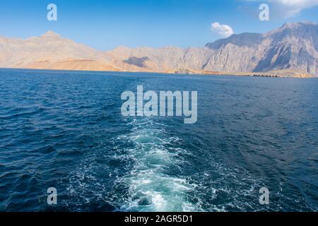 Blick von der Rückseite einer Dhow Boot mit Blick auf die Fjorde, schönen blauen Wasser, Berge und Wolken von Musandam, Oman im Nahen Osten. Stockfoto