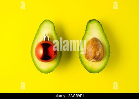Kreatives Konzept noch leben Ernährung Gesundheit Urlaub Foto von Avocado Hälften mit Weihnachten Spielzeug ball Dekoration auf gelben Hintergrund. Stockfoto