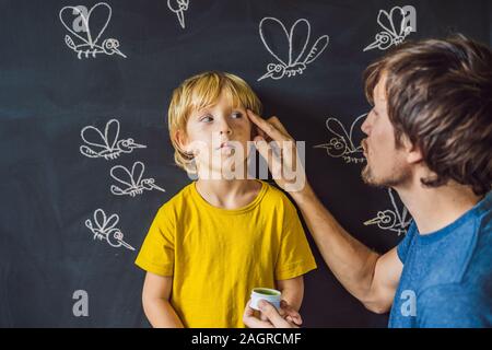 Der Junge wird durch Moskitos auf einem dunklen Hintergrund gebissen. Vati verschmiert sein biss Salbe. Auf der Tafel mit Kreide gemalt Moskitos Stockfoto