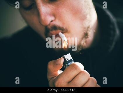 Ein bärtiger, sommersprossigen Mann in schwarzer Kleidung, der eine Zigarette mit der Flamme eines gas Feuerzeug. Stockfoto