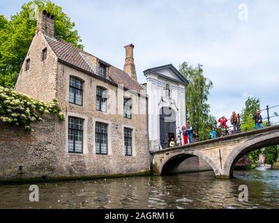 Menschen auf der Kanalbrücke und Eingangstor zum Begijnhof, Beginenhof in Brügge, Belgien. Stockfoto