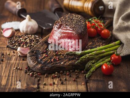 Ein Stück rohes Rindfleisch Oberschale mit Salz und Pfeffer auf Holz Schneidbrett mit Tomaten, Knoblauch und Spargelspitzen auf Holz Küche Tisch. Stockfoto