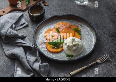 Buratta Käse mit Persimmon auf handgefertigten Teller serviert Stockfoto