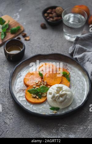 Persimone und buratta Käse mit Nüssen und Honig Stockfoto