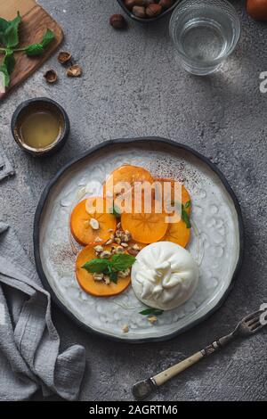 Buratta Käse mit Persimmon auf handgefertigten Teller serviert Stockfoto