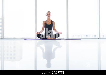 Das Mädchen übt Yoga in der Halle mit Panoramablick auf Windows Stockfoto