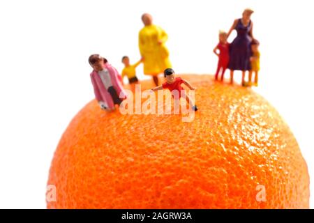 Minifigürchen Mama, Mütter, Kinder, Kinder, die auf einem orange Satsuma vor einem weißen Hintergrund Stockfoto