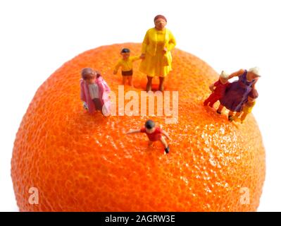 Minifigürchen Mama, Mütter, Kinder, Kinder, die auf einem orange Satsuma vor einem weißen Hintergrund Stockfoto