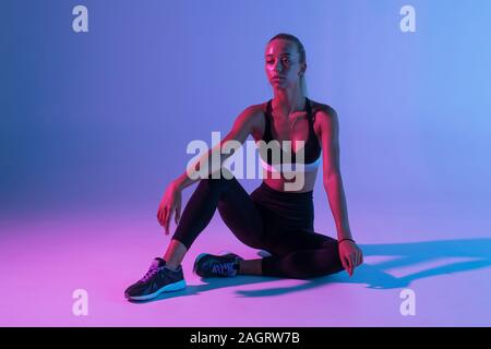 Portrait von attraktiven Frau mit schwarzen Anzug tun Gymnastik sitzen auf dem Boden isoliert über lila Hintergrund Stockfoto