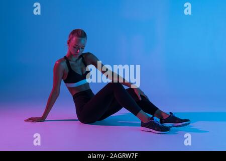 Portrait von attraktiven Frau mit schwarzen Anzug tun Gymnastik sitzen auf dem Boden isoliert über lila Hintergrund Stockfoto