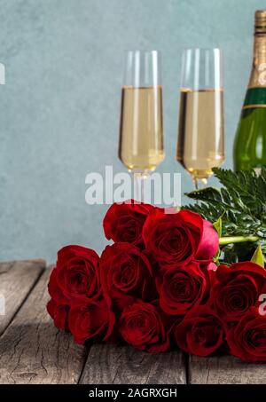 Blumenstrauß aus roten Rosen mit Champagner Gläser, im Hintergrund auf rustikalen Holztisch Stockfoto