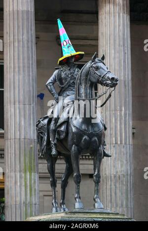 Glasgow, UK. 21. Dezember 2019. Am letzten Samstag vor Weihnachten einkaufen, Tausende von Kunden in Scharen in das Stadtzentrum von Glasgow auf die Straße Unterhaltung durch Govan Zweig der Heilsarmee, die internationale Lebensmittel auf den Märkten und die vielen executive Geschäfte in der Buchanan Street, Glasgow's tyle Meile" bekannt. Hier die Statue des Herzogs von Wellington hat die traditionelle respektlos Parkplatz Kegel mit einem in festlichen Farben ersetzt hatte. Credit: Findlay/Alamy Nachrichten Stockfoto