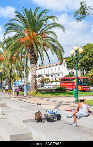 Funchal, Madeira, Portugal - Sep 10, 2019: City Promenade in der Hauptstadt Madeiras. Cobbled Pavement, grüne Vegetation, Palmen, einem Straßenhändler und die Menschen auf den Straßen. Sonnigen Tag. Stockfoto