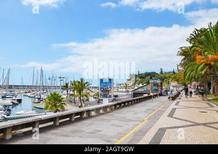 Funchal, Madeira, Portugal - Sep 10, 2019: City Promenade entlang des Hafens in der Hauptstadt Madeiras. Cobbled Pavement, grüne Vegetation, Palmen und die Menschen auf den Straßen. Boote im Hafen. Stockfoto