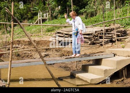 Weibliche touristische prekär Überqueren einer fadenscheinigen Schleifring Plank, ein Boot auf dem Mekong Fluss an Whisky Dorfs. Verbot Xiang Hai, Luang Prabang, Laos Stockfoto