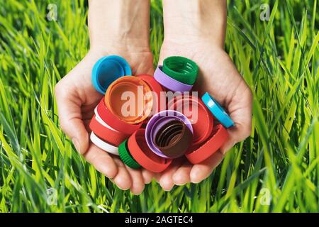 Schutzkappen aus Plastik von unterschiedlichen Flaschen in den Händen auf einem Hintergrund von Gras, close-up. Konzept zum Thema Respekt vor der Natur und Umwelt protecti Stockfoto