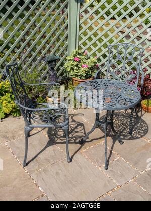 Metall Tische und Stühle auf einer kleinen Terrasse mit grünem Gitter, Topfpflanzen und Natursteinplatten in englischer Cottage Garten im Sommer. Stockfoto