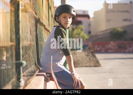 Portrait von modebewussten jungen Skater ruht sitzen Am Skatepark tragen Helm. Teenager genießt sonnigen Tag im Freien in der Stadt mit Skateboard. Jugend Stockfoto