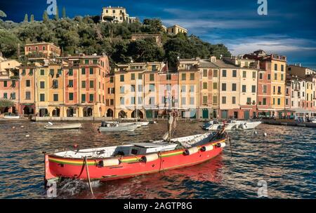 Kleine rote Fischerboot im Hafen von Portofino vor dem Hintergrund eines bunten alten Gebäuden entlang der Uferpromenade in einer malerischen Landschaft, Ligurien, Italien Stockfoto