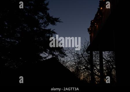 Weihnachten Kränze mit Kerzenlicht auf hölzernen Balkon in der Dämmerung in der Weihnachtszeit. Mit Baum umgeben und kleines Haus im Hintergrund. Niedrigen Winkel Stockfoto