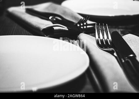 Tabelle Einstellung für Zwei mit leeren weißen Teller, Gabeln und Messer auf einem hölzernen Tisch im Restaurant. Schwarz und Weiß Foto Stockfoto