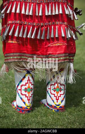 Details aus nächster Nähe zu roten Klingeltanzkostümen und Mokassinen, die von einer einheimischen Frau im Canada Day Powwow getragen wurden. Stockfoto