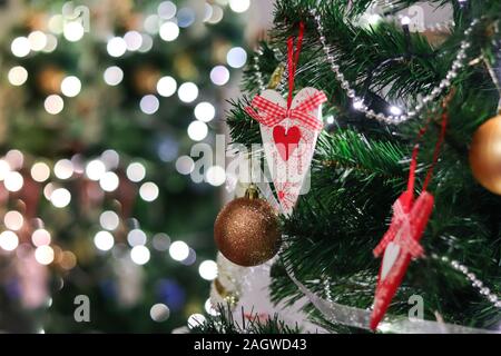 Geschmückten Weihnachtsbaum zu Hause mit roten Herzen Spielzeug und Lichter und Bokeh verschwimmt defokussierten Reflexion Hintergrund Platz für Text. Merry Xmas und Happ Stockfoto