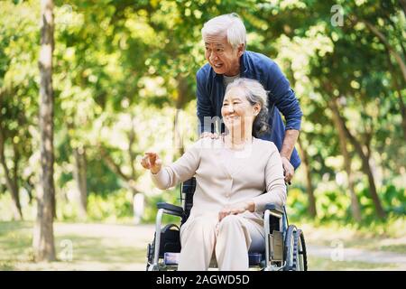 Senior asiatischer Mann und Rollstuhl gefesselt Frau Entspannung im Freien in Park Stockfoto